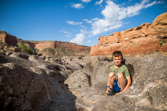 Young boy sits in rock depression while hiking near Moab, Utah