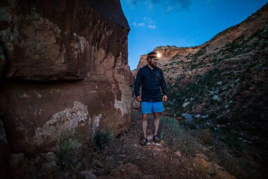 Hiker with headlamp stands on trail in rocky canyon