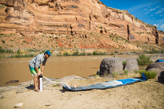 Man inflates stand up paddleboard on sandy riverbank