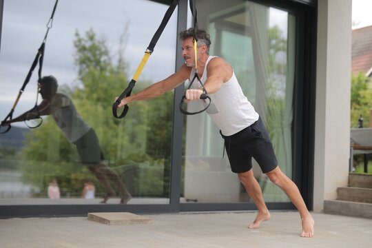 Fit mature man doing suspension training on a patio
