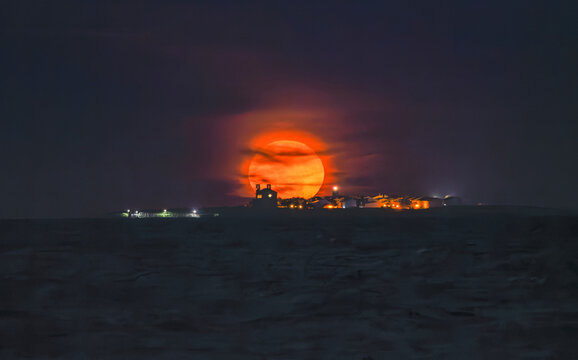 Huge orange full moon perfectly aligned behind Tabarca Island at night