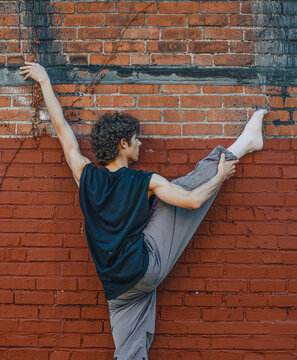 Male dancer holds a standing split against a brick wall