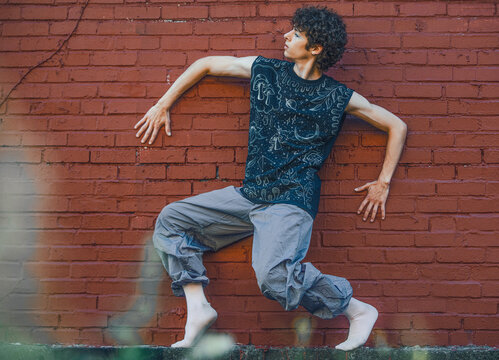 Young man in a dynamic dance pose against a brick wall