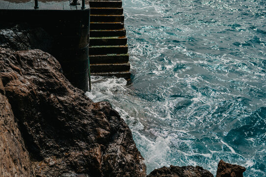 Stone stairs descending into choppy blue water at Ponta do Sol