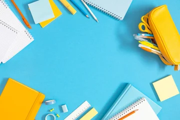 Bright Back to School Flat Lay Frame with Yellow Pencil Case, Notebooks, and Stationery Around Central Copy Space on Light Blue Background. Colorful Office and Education Layout. Top View. © prime1001