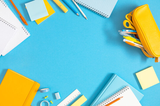 Bright Back to School Flat Lay Frame with Yellow Pencil Case, Notebooks, and Stationery Around Central Copy Space on Light Blue Background. Colorful Office and Education Layout. Top View.