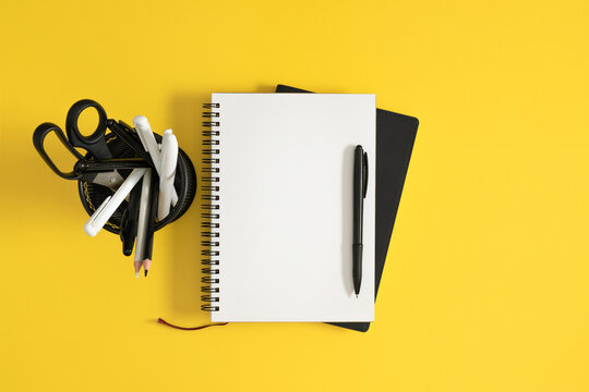 Horizontal Flat Lay with Open Blank White Notebook, Black Pen, and Desk Organizer on Bright Yellow Background. Minimalist Contrast Office and Back to School Stationery Layout. Top View.