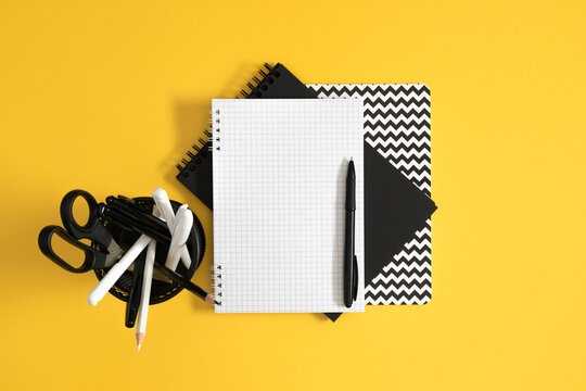Horizontal Flat Lay with Blank Grid Notebook, Black Pen, and Chevron Pattern Notepad on Bright Yellow Background. Contrast Minimalist Office and Back to School Stationery Layout. Top View.
