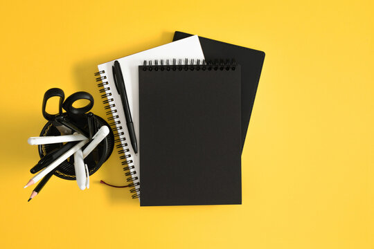 Horizontal Flat Lay with Blank Black Cover Notebook, Open Notepad, and Stationery Organizer on Bright Yellow Background. Contrast Minimalist Office and Back to School Concept. Top View.