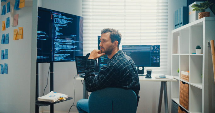 Young Caucasian male programmer write creative plan on whiteboard and coding on computer in home office workspace. AI technology, cybersecurity network, agile strategy, business innovation concept.