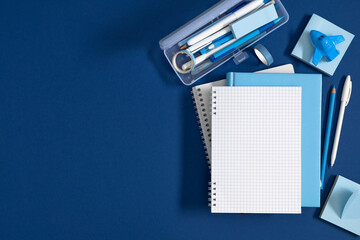 Blue Stationery Flat Lay with Blank Grid Notebook, Pencil Case, Pens, and Toy Airplane on Dark Blue Background. Back to School, Office, and Education Concept with Copy Space. Top View Layout. © prime1001