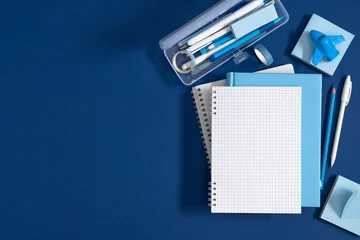 Blue Stationery Flat Lay with Blank Grid Notebook, Pencil Case, Pens, and Toy Airplane on Dark Blue Background. Back to School, Office, and Education Concept with Copy Space. Top View Layout. © prime1001