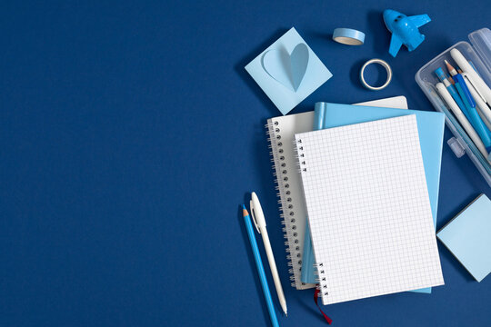 Blue Stationery Flat Lay with Blank Grid Notebook, Pencil Case, Pens, and Heart Notes on Dark Blue Background. Back to School, Office, and Education Concept with Left Side Copy Space. Top View.