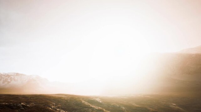 A bright sunrise rises over distant mountains while fog rolls through the valley. Soft light fills the scene as day breaks. The landscape is quiet as the sun begins to warm the ground.