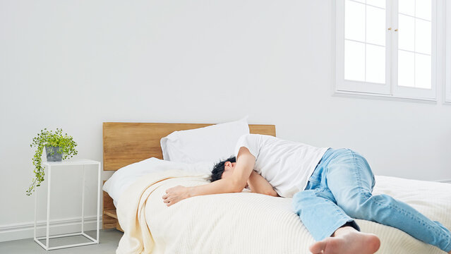 ベッドに寝転がる男性。寝不足、不眠症、落ち込む、がっかり、悩む、ストレス、昼寝、疲労、不安、寝坊