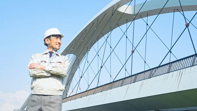橋の前で遠くを眺める男性作業員。建設、工事、インフラ、点検、検査、メンテナンス、保守、安全、修理