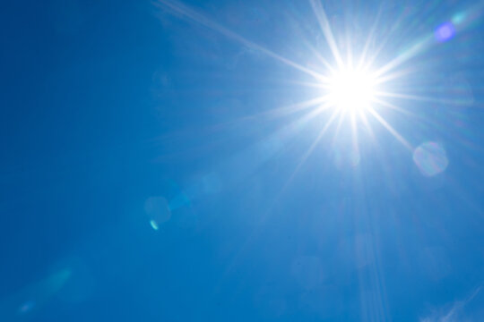 Bright sun shining in the upper right corner of a clear blue sky creating a beautiful starburst with lens flare