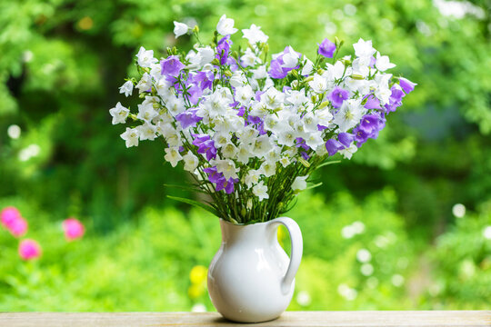 Jar of colorful canterbury bell flowers on wooden table in a garden