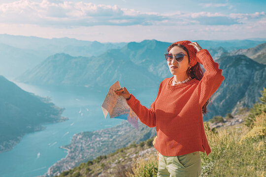 Woman standing on a mountaintop, holding a map, feeling confused and lost while traveling in Montenegro