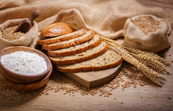 fresh bread, bowl of flour, wheat grains and spikelets on wooden table