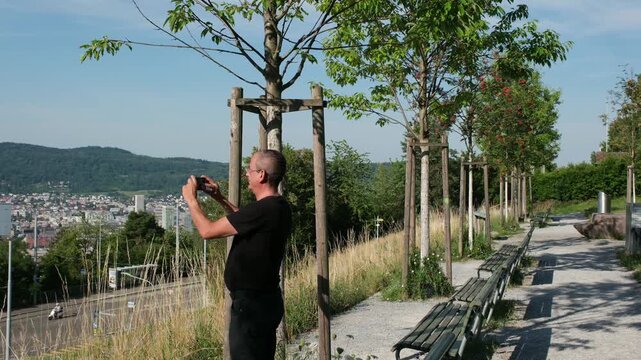 Mann fotografiert mit Mobiltelefon das Stadtpanorama von Z&uuml;rich, Fotos mit dem Handy machen, Freizeit Aktivit&auml;t im Sommer