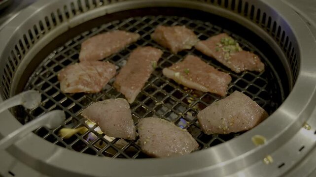焼肉屋にて和牛カルビと厚切りタンを焼き、トングで裏返しするシーン