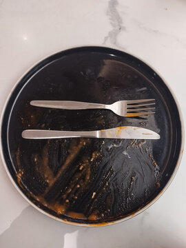 A dirty, empty plate with a fork and knife on it. The dirty, empty plate is isolated against a black background.