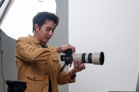 Asian male photographer adjusting professional camera with telephoto lens in studio