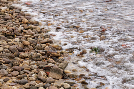 Foaming ocean waves washing over smooth beach pebbles