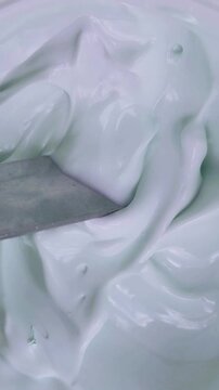 Vertical top down view of stirring cream slowly with a spoon in top to bottom motion. Beauty product concept, smooth thick texture for skincare preparation.