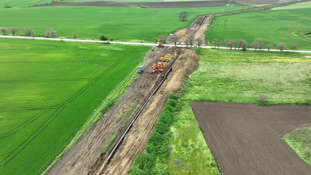 Aerial view of a major pipeline construction project. Heavy machinery including excavators and pipelayers install a new gas line in a rural field. Industrial energy infrastructure development.