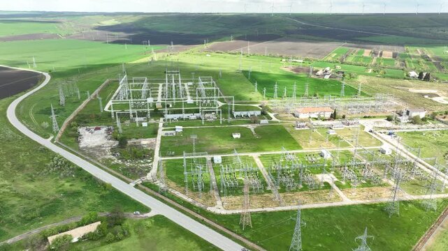 Aerial view of an electrical substation and high-voltage power lines with a wind farm on the horizon. Energy grid infrastructure, symbolizing the transition to renewable power.