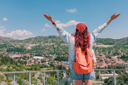 Backpacker woman raising arms celebrating freedom and adventure with a scenic view of Cetinje town and mountains in Montenegro