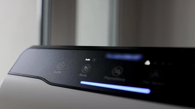 close-up shot of a male finger touching the electronic control panel or touch button of a modern black air purifier machine to turn it on or change settings.