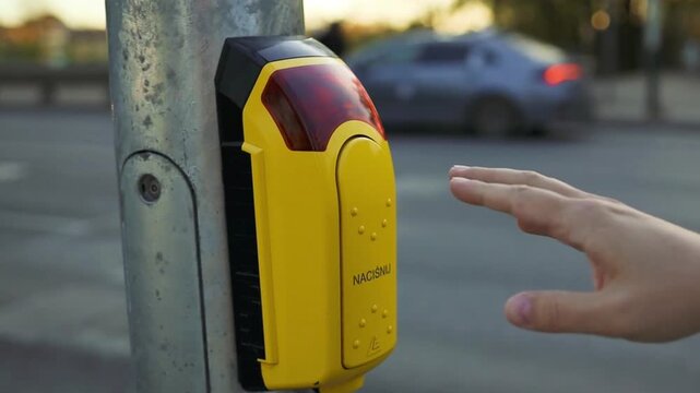 close-up of hand pressing yellow button on urban street side view, neutral mood, plastic and metal pole, commercial and public transportation setting, yellow button and metal pole, neutral.