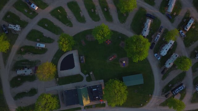 Wisconsin RV park at dusk &mdash; campsite spokes fanning around a green commons with swimming pool, playground, pavilion, and rows of parked campers and trailers.