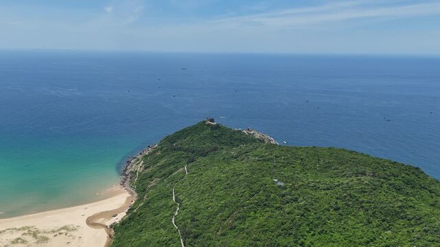 Drone footage captured flying from inland toward the coast along a scenic hillside in Dak Lak (formerly Phu Yen) Province, Vietnam. The aerial view gradually reveals Bai Mon Beach on the left