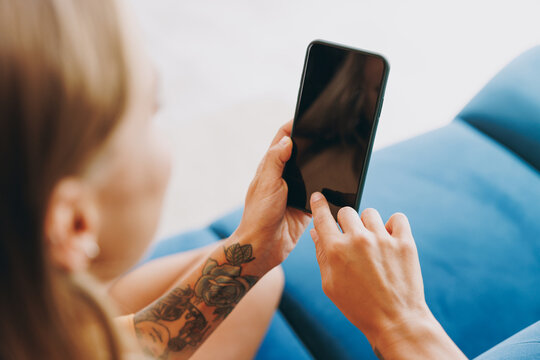 Cropped young woman wears casual clothes hold use mobile cell phone with blank screen workspace area sits on blue sofa couch stay at home hotel flat rest relax spend free time in living room indoor.