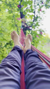 Vertical video of a person relaxing in a hammock among beautiful flowers and trees