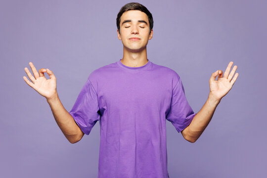 Young Caucasian man wear violet t-shirt casual clothes hold spreading hands in yoga om aum gesture relax meditate try to calm down isolated on plain pastel light purple background. Lifestyle concept.