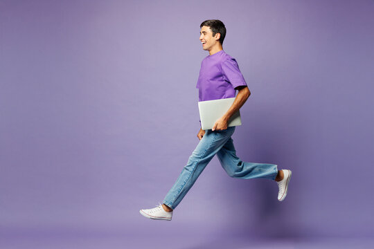 Full body side view young fun IT man wear violet t-shirt casual clothes jump high run hold closed laptop pc computer isolated on plain pastel light purple background studio portrait. Lifestyle concept