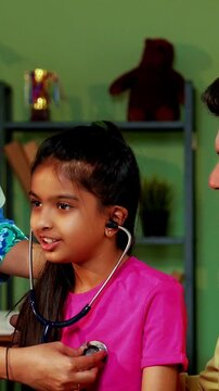 Indian Asian playful female doctor or pediatrician engaging young girl patient by letting her hear own heartbeat using stethoscope in a warm and friendly clinic atmosphere
