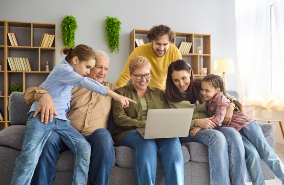 Family grandparents parents children using laptop together. The smiling group bonding at home, exploring technology, video calling, and learning online. Clear concept: digital family bond.