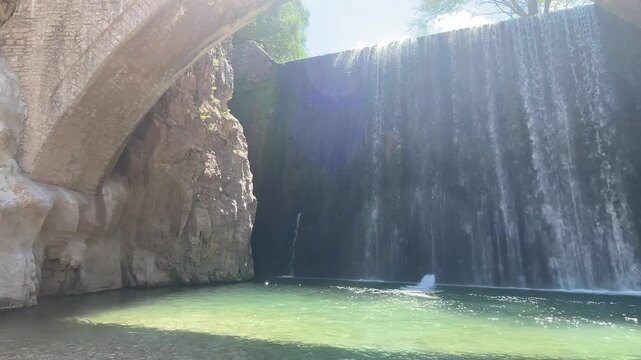 Paleokaria stone arched bridge and beautiful waterfall cascading into emerald green river pool on sunny day in Trikala region Greece. High quality footage