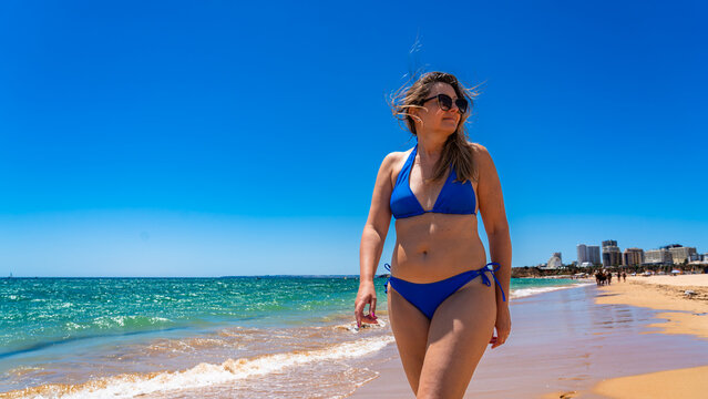 Beautiful middle-aged woman sunbather walking on sandy beach in summertime. Front view
