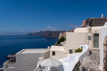 Obraz premium Traditional Cycladic architecture with white buildings and stone pathways on a cliffside in Oia, Santorini. Deep blue Aegean Sea and volcanic cliffs under a clear sunny sky.