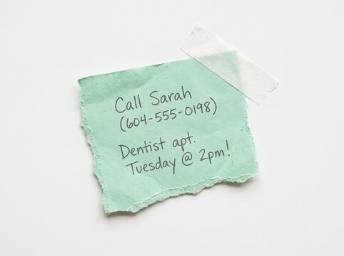 Realistic green torn paper note with handwritten dentist appointment reminder, call Sarah message and phone number, taped to white background for mockup. Isolated memo scrap with masking tape.