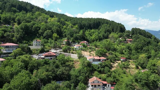 Drone aerial view of Ropoto village houses with red roofs on steep mountain slopes covered with dense green forest in Thessaly region at sunny summer day. High quality 4k footage
