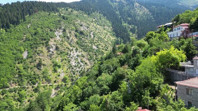 Drone aerial view of Ropoto village houses with red roofs on steep mountain slopes covered with dense green forest in Thessaly region at sunny summer day. High quality 4k footage