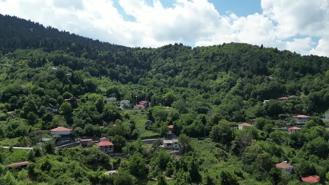 Drone aerial view of Ropoto village houses with red roofs on steep mountain slopes covered with dense green forest in Thessaly region at sunny summer day. High quality 4k footage